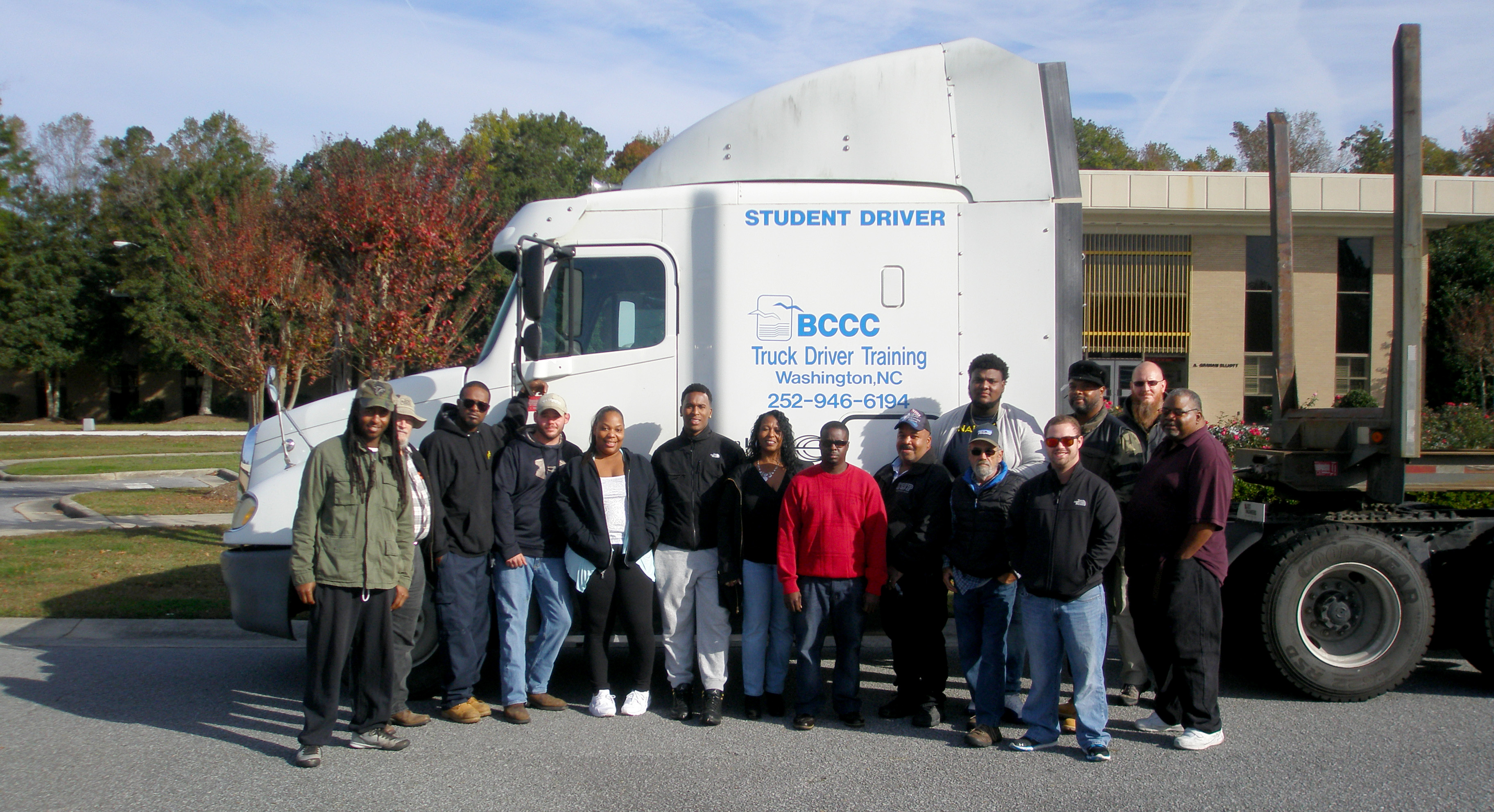 A dozen students stand in front of a truck cab in front of the college.