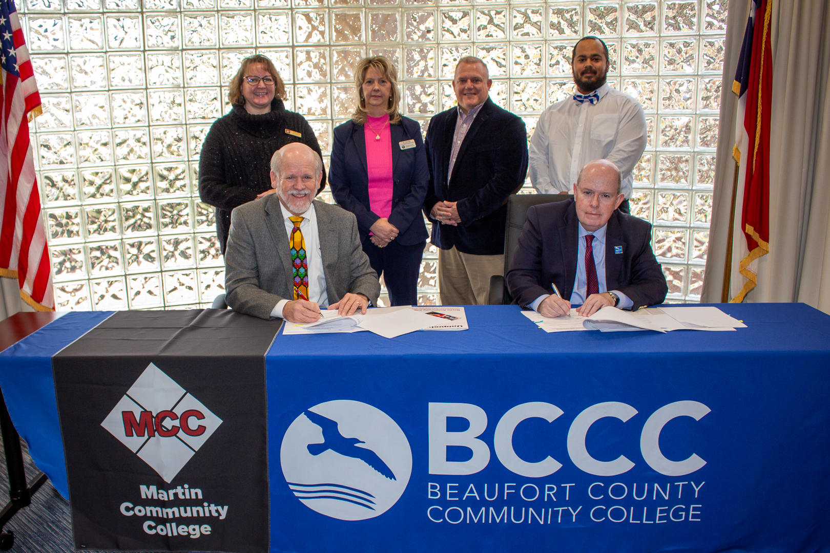 2 people signing documents and 4 people looking banners say martin county community college beaufort county community college