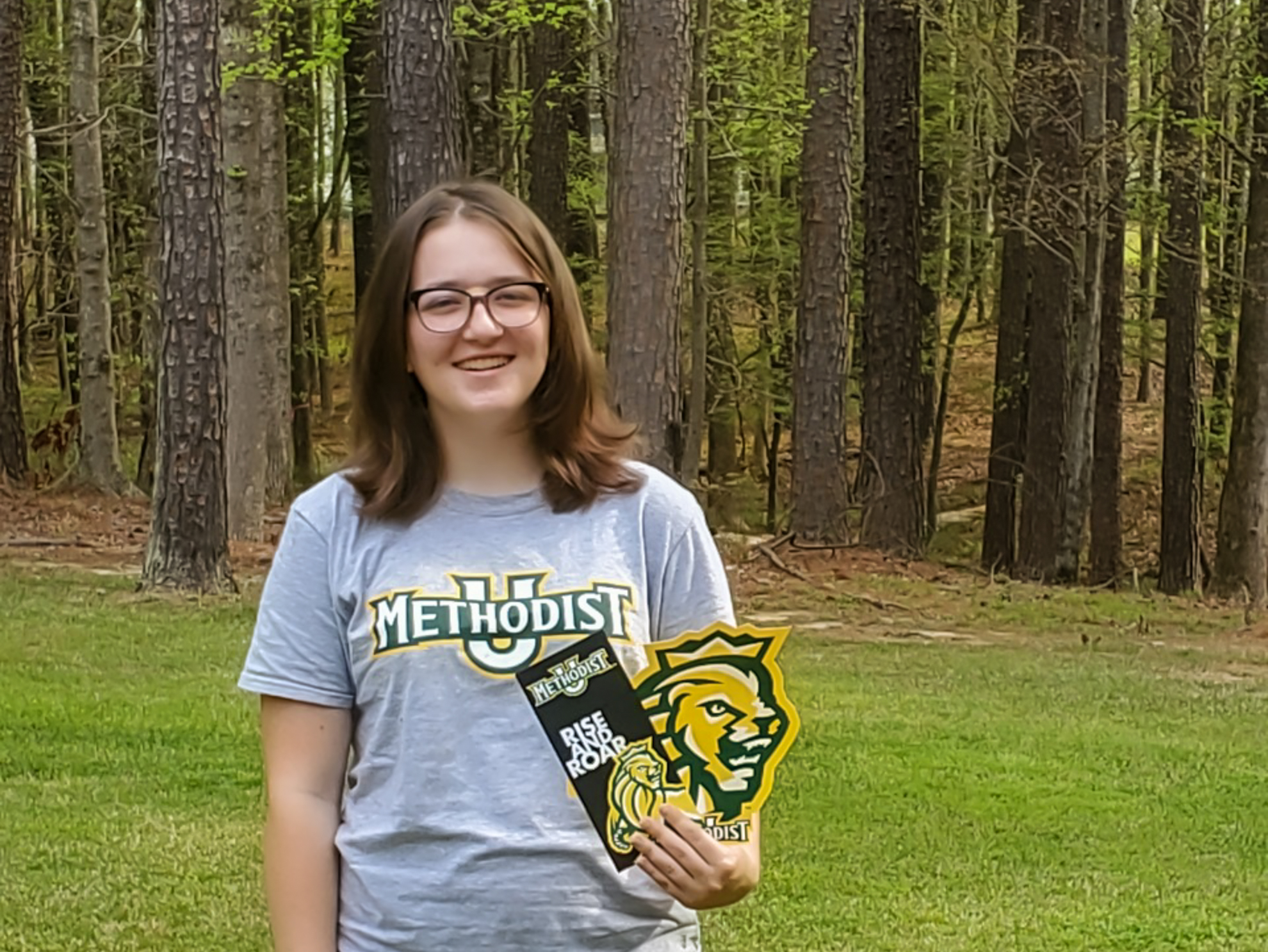 a student with a methodist U shirt holding a card that reads rise & roar
