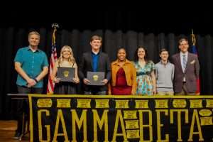 Group of people on stage with Gamma Beta Phi banner.