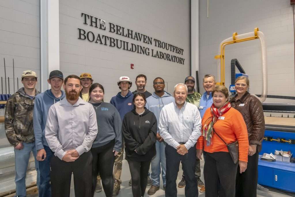 People in large shop with sign saying "The Belhaven Troutfest Boatbuilding Laboratory."