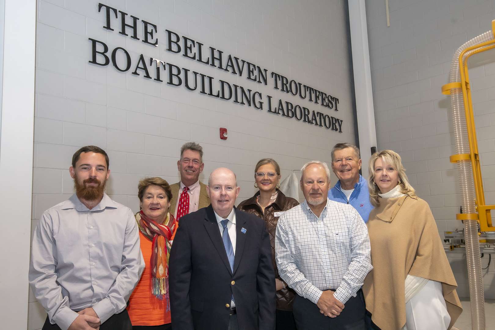 People in front of a sign, text reading The Belhaven Troutfest Boatbuilding Laboratory