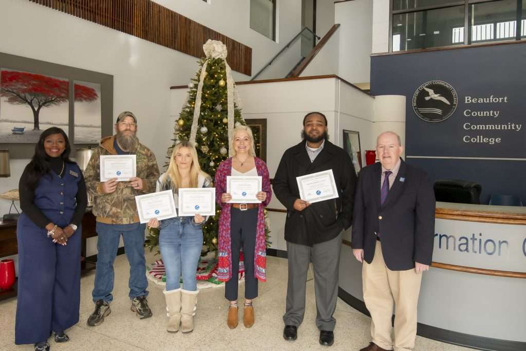 a group of students with awards and administrators. holiday decorations