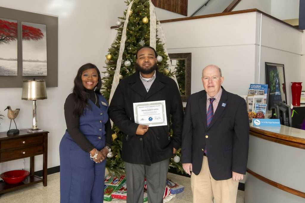3 people in front of a holiday tree, one holding an award