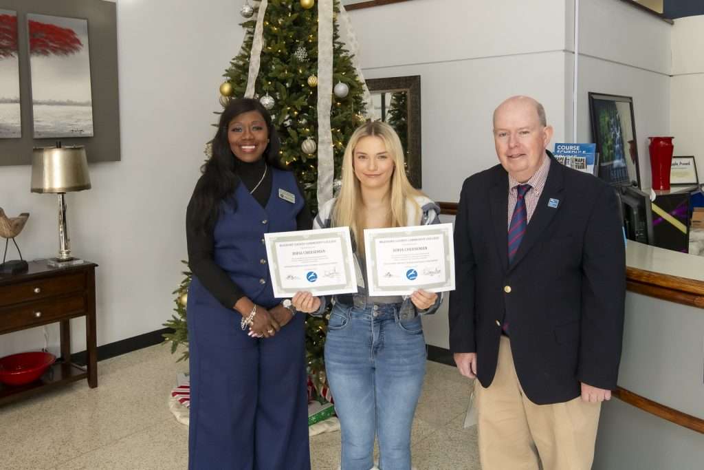 person holding two awards with two administrators in front of Christmas tree