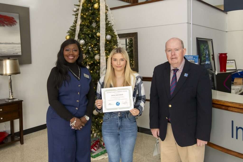 3 people in front of a christmas tree, one holding an award